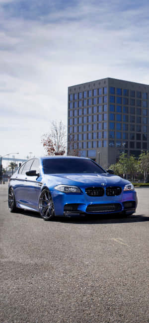藍色BMW M5停在辦公大樓附近的城市街道上。 — Galaxy A15 壁紙
