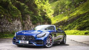 藍色 Mercedes-AMG GT Roadster 停泊在風景優美的山路上，兩旁是綠色的山坡。