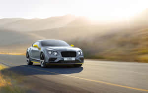 銀色賓利 Continental GT 在日出時於沙漠公路上疾馳。