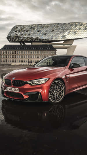 紅色BMW M4跑車停在潮濕路面上，背景有現代建築。 — iPhone 8 壁紙