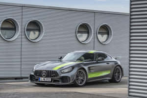灰色Mercedes-AMG GT跑車，帶有綠色點綴，停在工業建築附近。