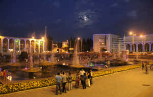 夜晚的城市廣場，燈光噴泉和人們在月光下享受場景。