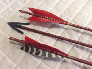 三支手工製作的箭，帶有紅色和圖案箭羽，放在絎縫布料上。