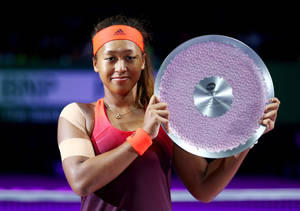 網球選手手持一個帶有紫色紋理表面的大型銀色獎盃。