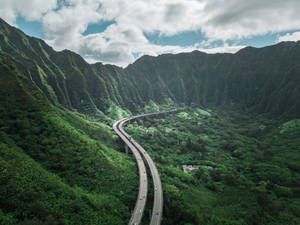 一條彎曲的高速公路在多雲的天空下穿過茂密的綠色山谷。 — 道路 壁紙