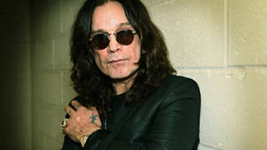Ozzy Osbourne 戴住太陽眼鏡靠喺混凝土牆上，紋身清晰可見。