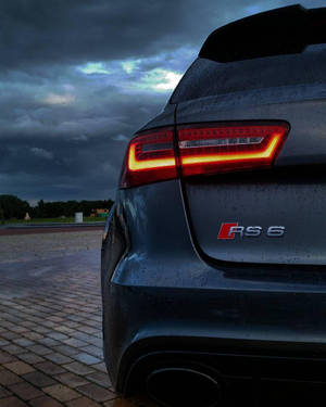 深灰色奧迪RS6房車在暴風雨天空下的潮濕磚路上，亮起發光尾燈。 — Audi R8 GIF 壁紙