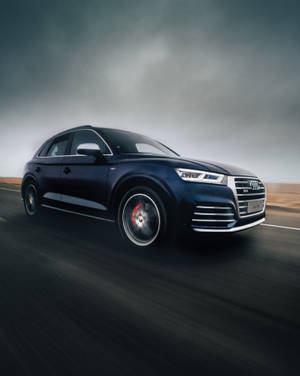 深藍色 Audi SQ5 SUV 在潮濕的道路上疾馳，天空多雲。
