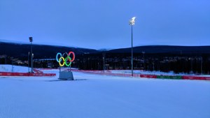 黃昏時分，奧運五環在白雪覆蓋的斜坡上發光，背景有山巒。