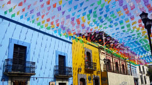 色彩繽紛的 papel picado 橫幅掛在節日街道上，街道上有藍色和黃色的建築。