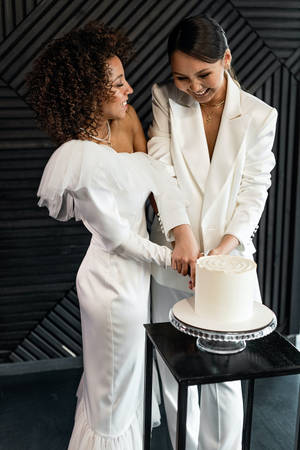 兩位身穿白色婚紗的新娘在室內切結婚蛋糕。