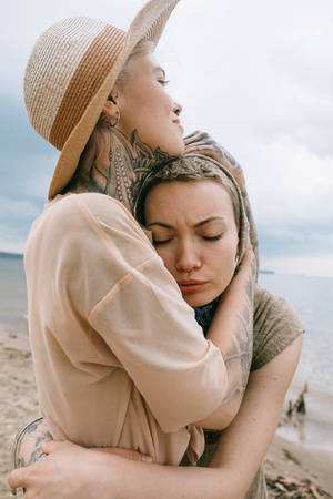 兩位紋身女士在海灘上擁抱，身後是海浪。