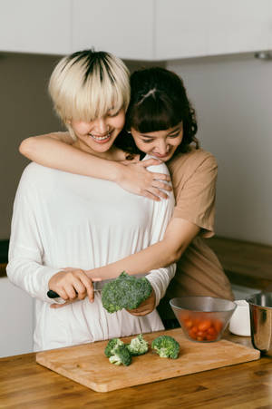 兩位女性在廚房準備西蘭花時擁抱。