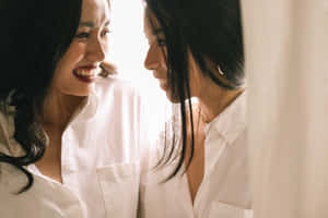 兩位身穿白恤衫的女性在柔和光線中溫暖地微笑相對。