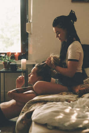 兩名女子在臥室中，一人為另一人編辮子，同時手持香煙。