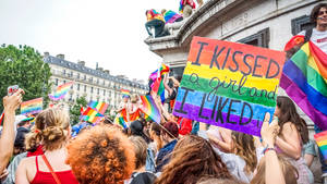 Pride遊行中揮舞彩虹旗和手持標語牌的人群。