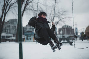 在雪地城市公園中穿著冬季衣服坐在鞦韆上的人