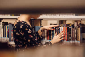 紅指甲女性在圖書館書架上瀏覽書籍。