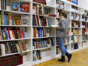 女人在圖書館通道中瀏覽書籍，白色書架和木地板。