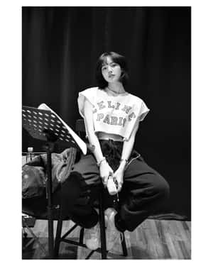 年輕女性穿著休閒服裝，坐在攝影棚內音樂架旁的凳子上。