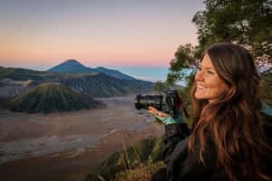 女性手持相機在火山群山上日出時微笑。