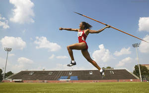 身穿紅色運動服的女運動員在陽光明媚的日子在戶外體育場擲標槍。