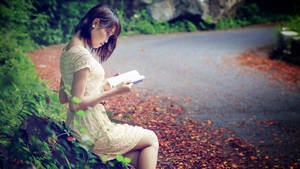 女性在秋天落葉覆蓋的小徑上閱讀一本書。