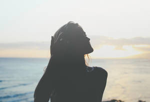 女人喺海邊日落中嘅剪影，手放喺頭度。