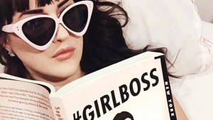 戴白色太陽眼鏡的女性在床上閱讀 Girlboss 書籍