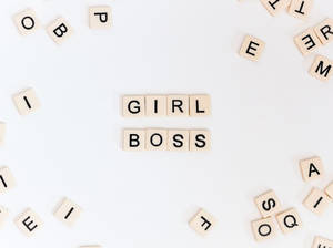 木製拼塊在白色背景上拼出 girl boss，周圍散落字母。