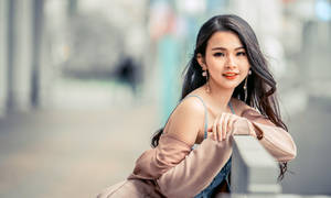 一位穿著粉紅色外套的微笑女性在城市街道上倚靠欄杆。