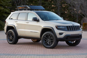 米色Jeep Grand Cherokee，黑色輪圈和車頂行李架，停在磚砌車道上。