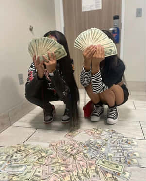 兩名女孩蹲在走廊上，用扇形的美元鈔票遮住臉，地上有現金。