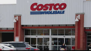Costco Wholesale 商店入口，有停泊的汽車和多雲的天空。