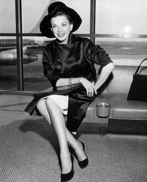 1950年代時尚女性在機場客運大樓窗邊微笑，窗外有飛機。