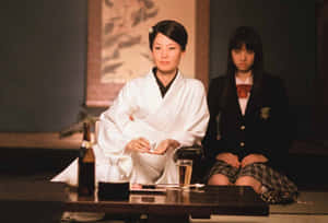 兩位穿著傳統服裝和校服的女性在室內矮桌旁就座。