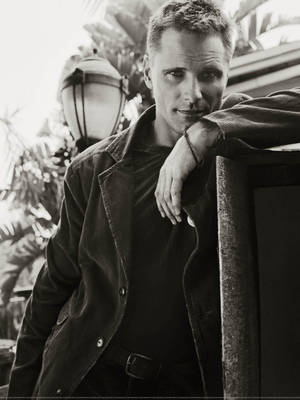 一個穿著深色外套的男人靠在欄杆上，身後有棕櫚樹和燈籠。