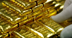 戴著手套的手觸摸一堆閃閃發光的金條。 — 金色美學 GIF 壁紙