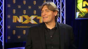 黑西裝男子在WWE NXT工作室環境中微笑。