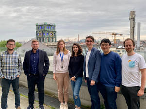 六個微笑嘅人喺城市屋頂上擺姿勢，背景有鐘樓。