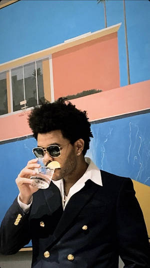 身穿海軍藍西裝的男士在彩色壁畫牆前啜飲帶檸檬的飲品。