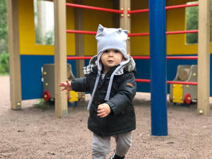 一個戴著貓耳帽和冬季外套的幼兒在遊樂場上。