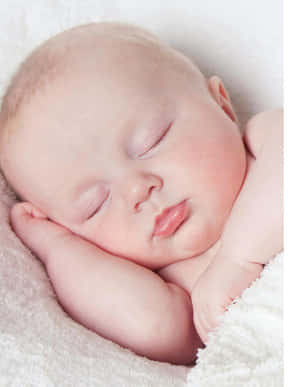 一個睡著的新生嬰兒，雙手放在下巴下，躺在蓬鬆的白色毯子上。
