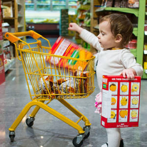一個幼兒在雜貨店推著一輛裝滿零食的黃色購物車。
