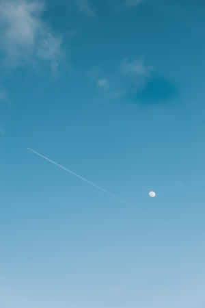清澈藍天中的月亮和飛機雲，伴隨柔軟雲朵