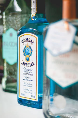 白色表面上藍色 Bombay Sapphire 氈酒瓶，背景瓶子模糊。