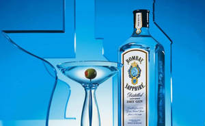 Bombay Sapphire氈酒瓶和帶橄欖的馬提尼酒杯在藍色背景上