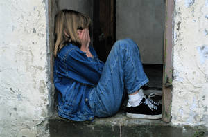 一個穿著牛仔布的女孩坐在門口時遮住臉。