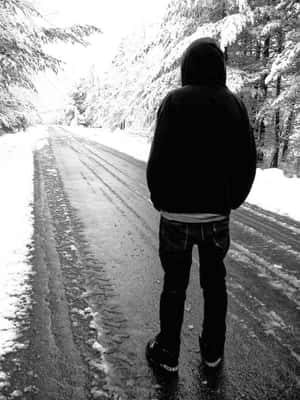 穿連帽衫的人獨自站在雪路上，被積雪的樹木包圍。