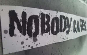 一張黑色模板貼紙，上面寫著「NOBODY CARES」，貼在帶有墨水飛濺的灰色牆上。